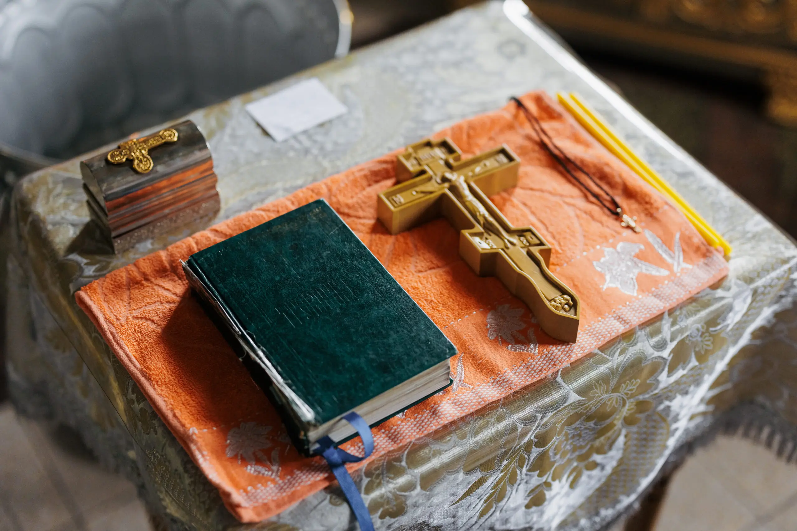 Close-up of an Orthodox Bible, golden crucifix, and candles placed on an altar table inside a church. Symbol of faith, religious ceremony, prayer, and sacred Christian tradition.
