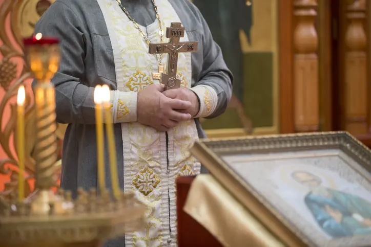 Priest's hand with a cross on the background of church candles.