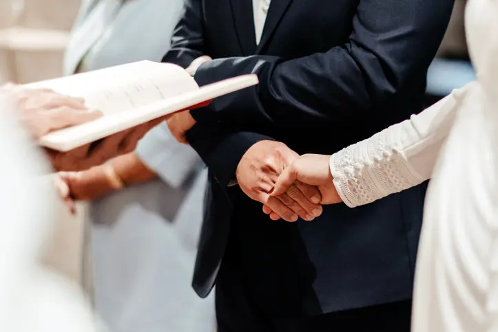 Detail of a couple holding hands at the altar during the wedding ceremony in front of the priest. Catholic sacrament of marriage in church